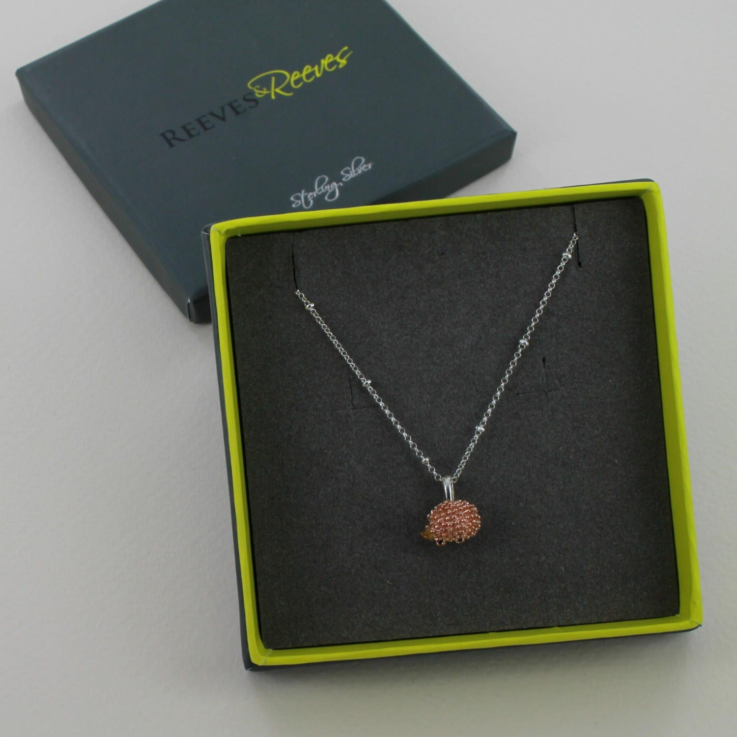 Hedgehog Pendant in rose gold, shown on a silver adjustable chain and in a Reeves & Reeves branded gift box in grey and green colours.