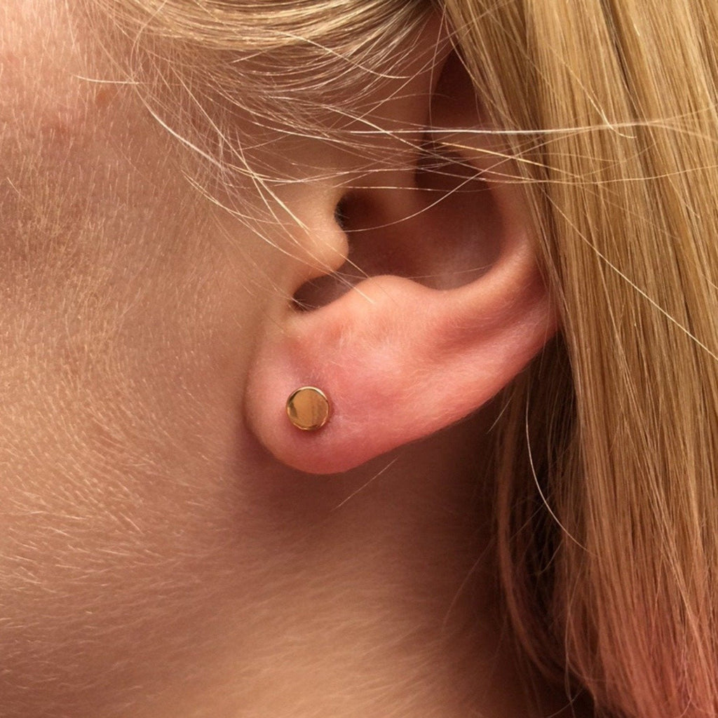 An 18ct gold plated high shine circle stud, shown in a ladies ear.