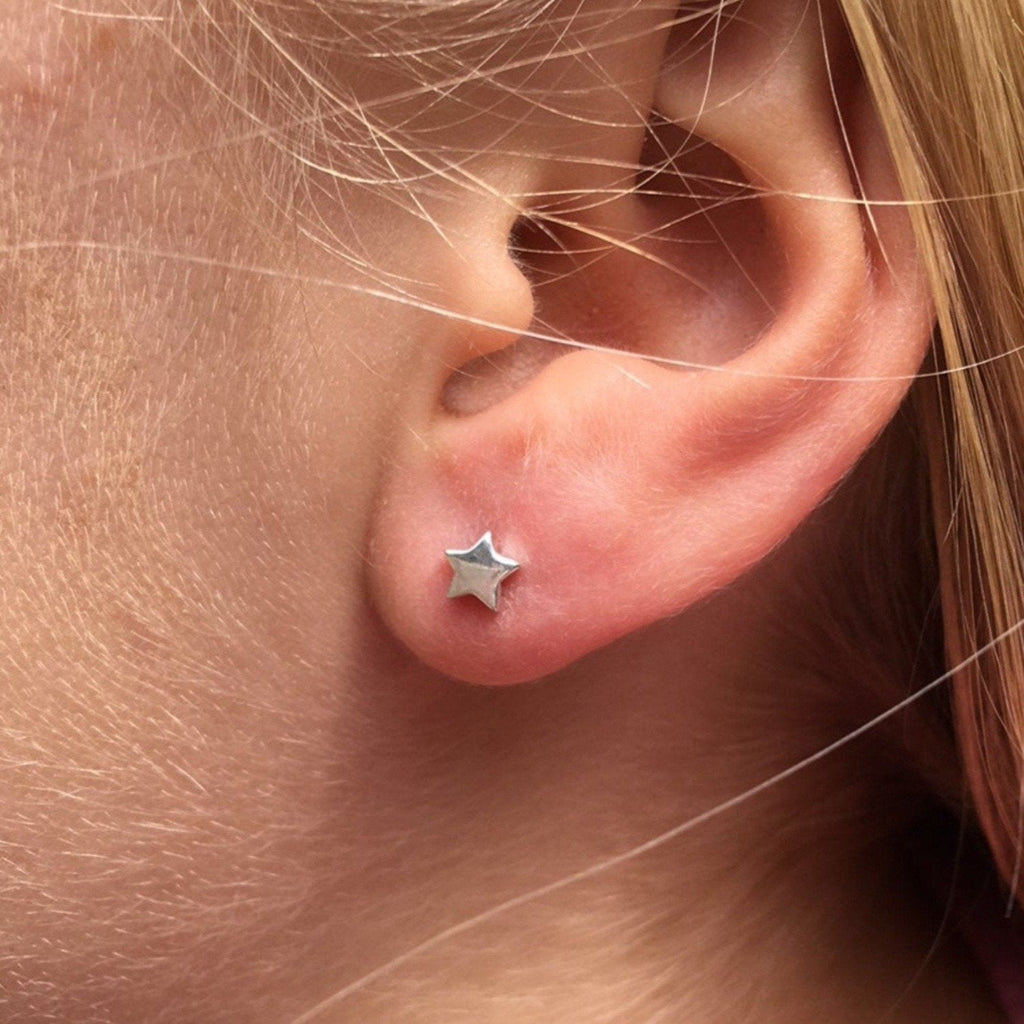 A pair of sterling silver star stud earrings, shown in a ladies earlobe.