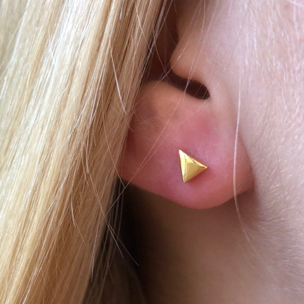 A gold plated triangle stud earring, shown in a ladies ear.