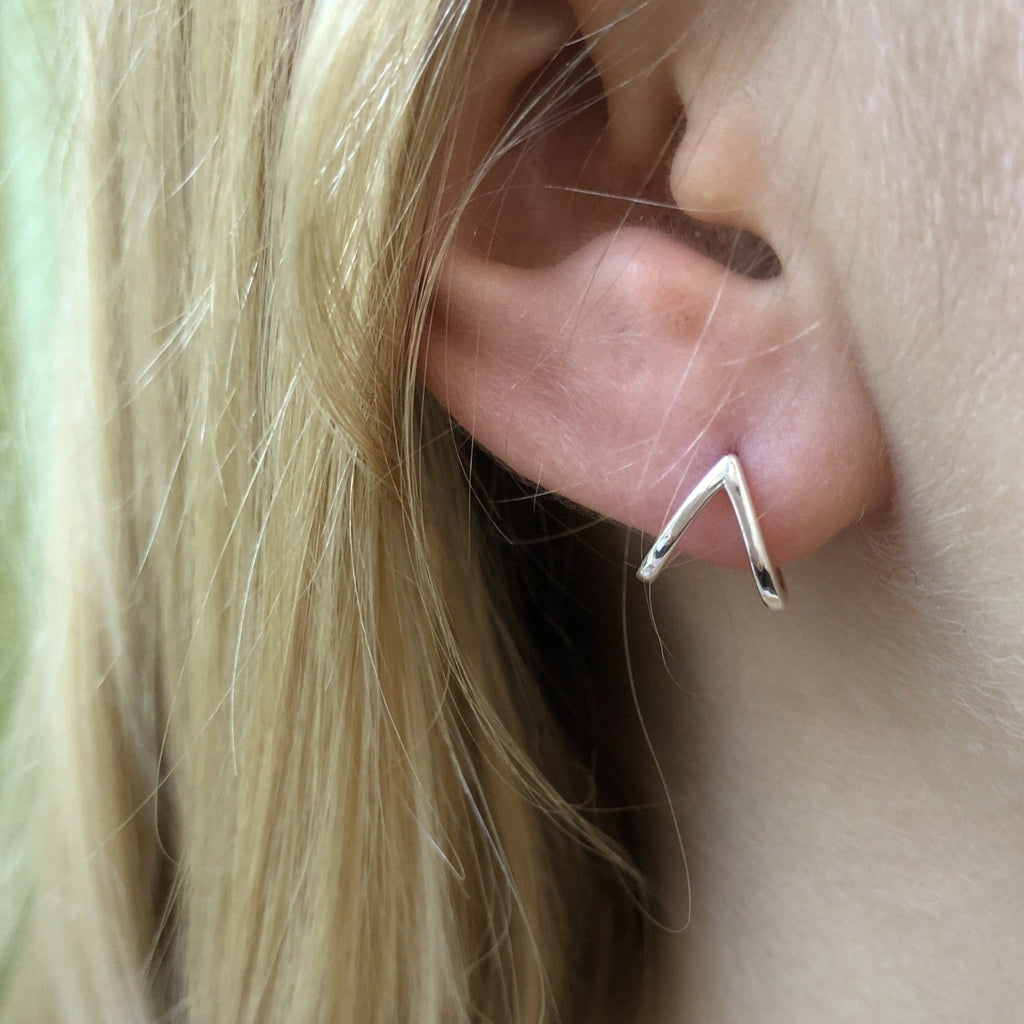 A sterling silver heart huggie, shown in a ladies ear.