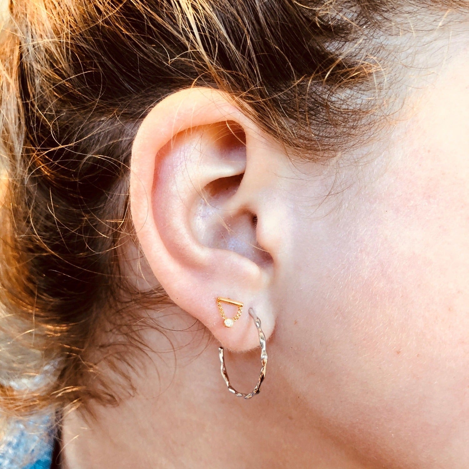 A pair of sterling silver hoop earrings, shown in a ladies ear.