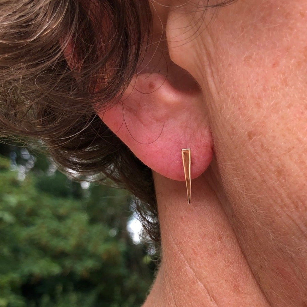 An iso triangle stud earring with gold plating and shown in a ladies ear.