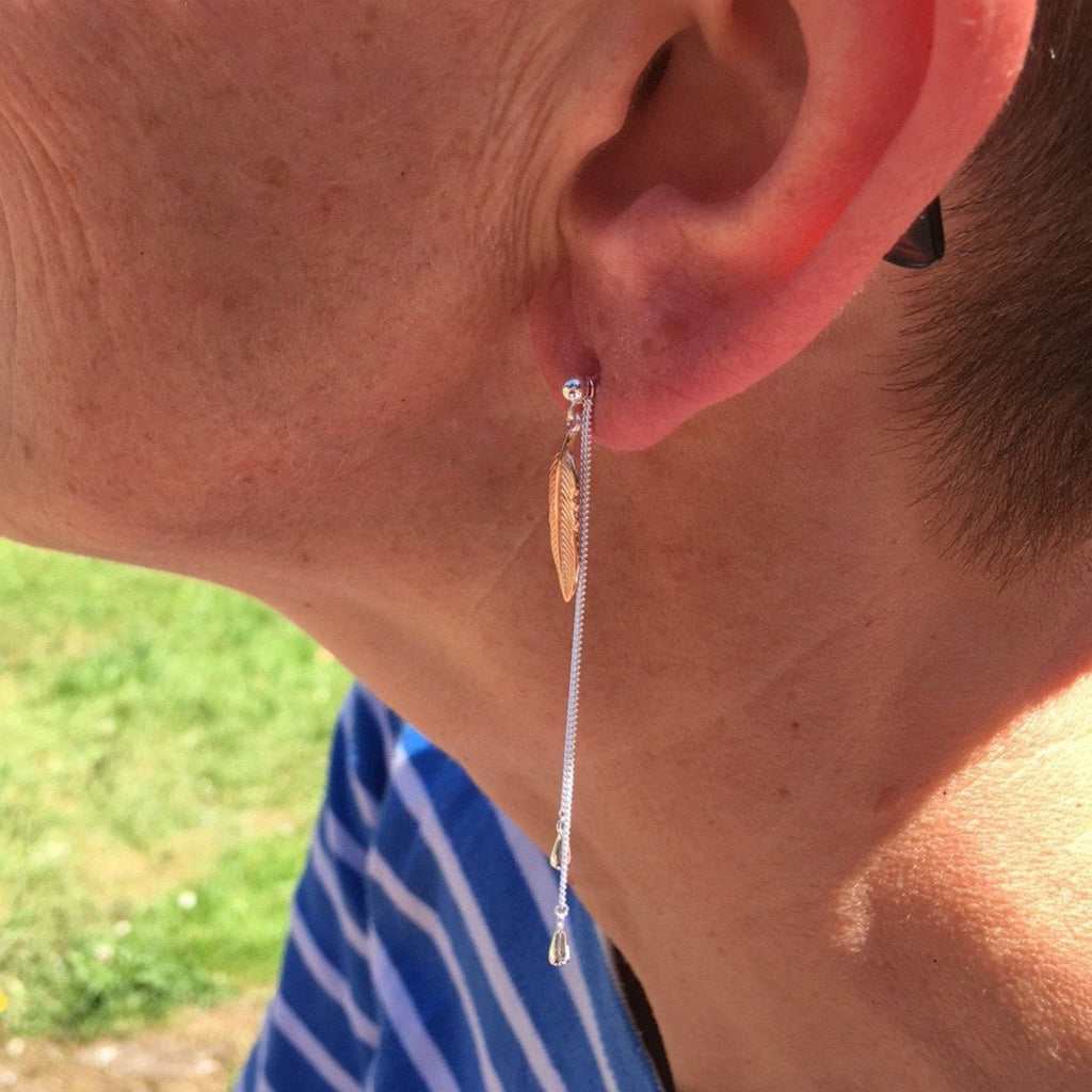 A stud style post with a leaf hanging from the stud and two fine chains hanging behind. Shown in a ladies ear.