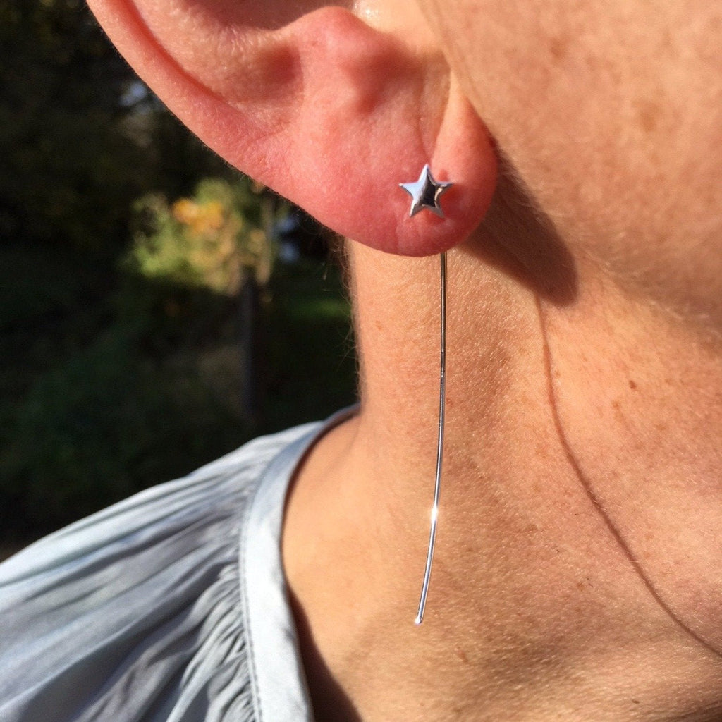 A sterling silver star earring with a long pull through back which sits behind the ear. Worn in a ladies ear.