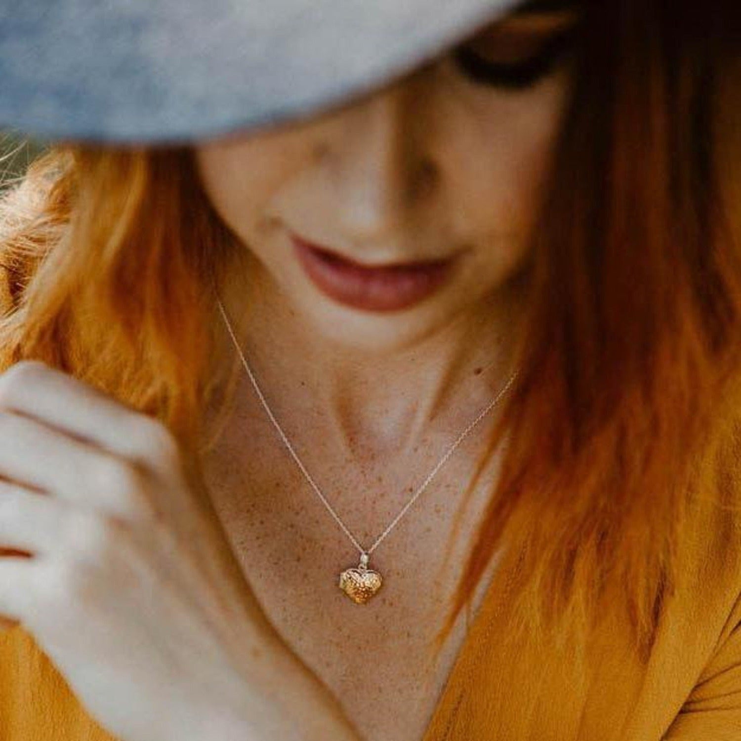 A heart shaped locket with a slightly hammered texture, hanging on an adjustable silver chain and worn on a models neck.