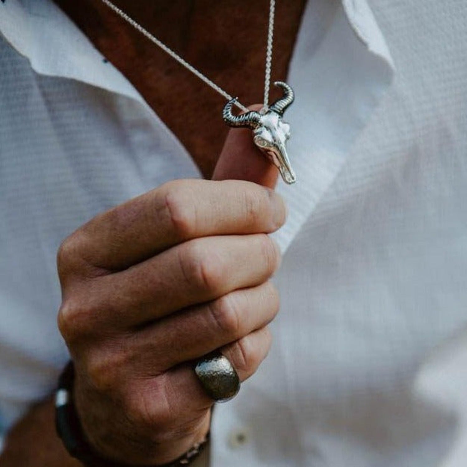 A Silver wildebeest pendant with black ruthenium horns and hanging on a silver chain, worn on a man.