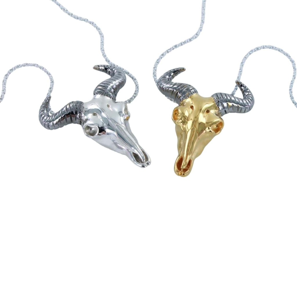 Two sterling silver pendants in the shape of wildebeest skulls, one with a silver finish and the other with a gold vermeil finish, on textured chains.