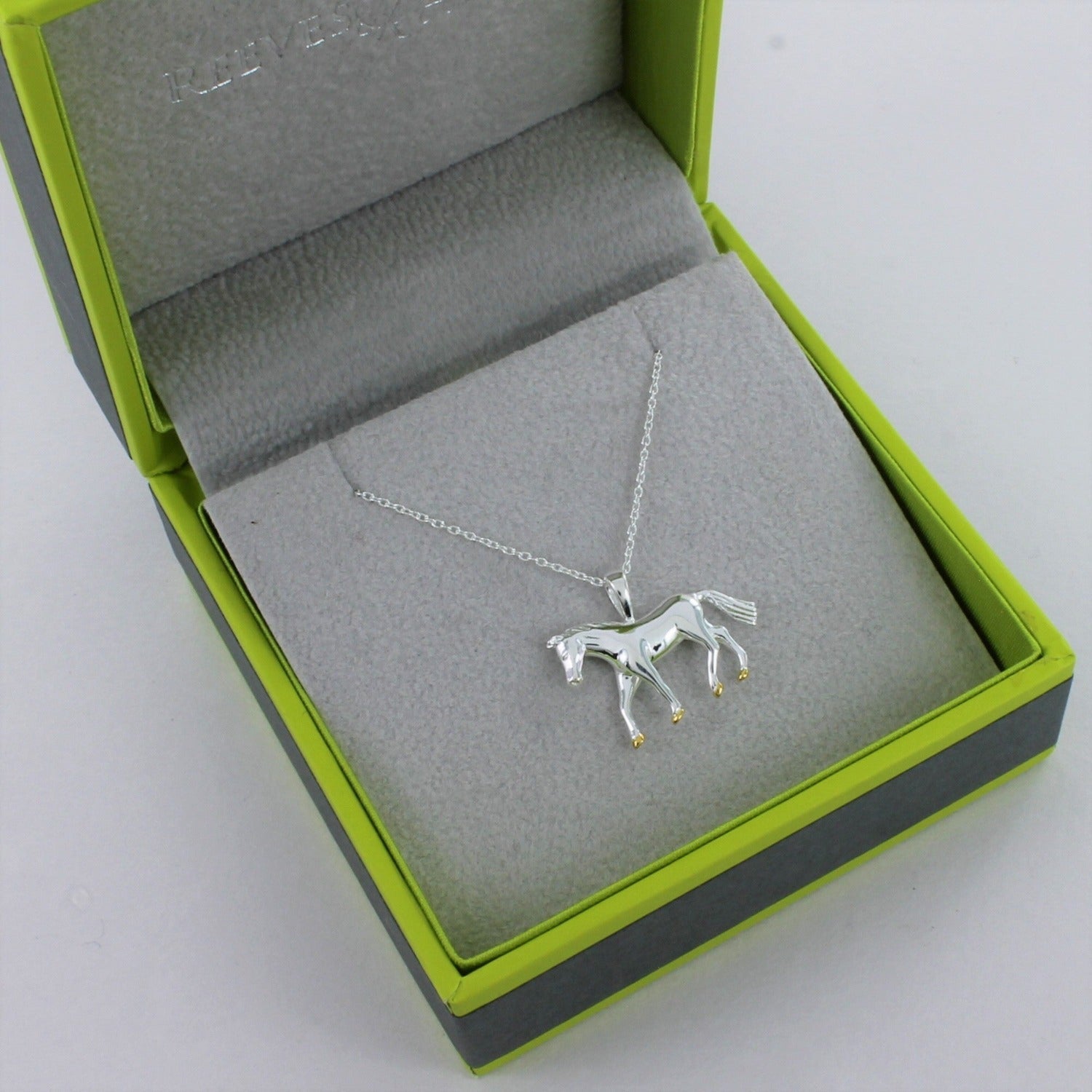 A sterling silver horse pendant with gold plated hooves hanging on a silver adjustable chain and shown in a Reeves & Reeves gift box.