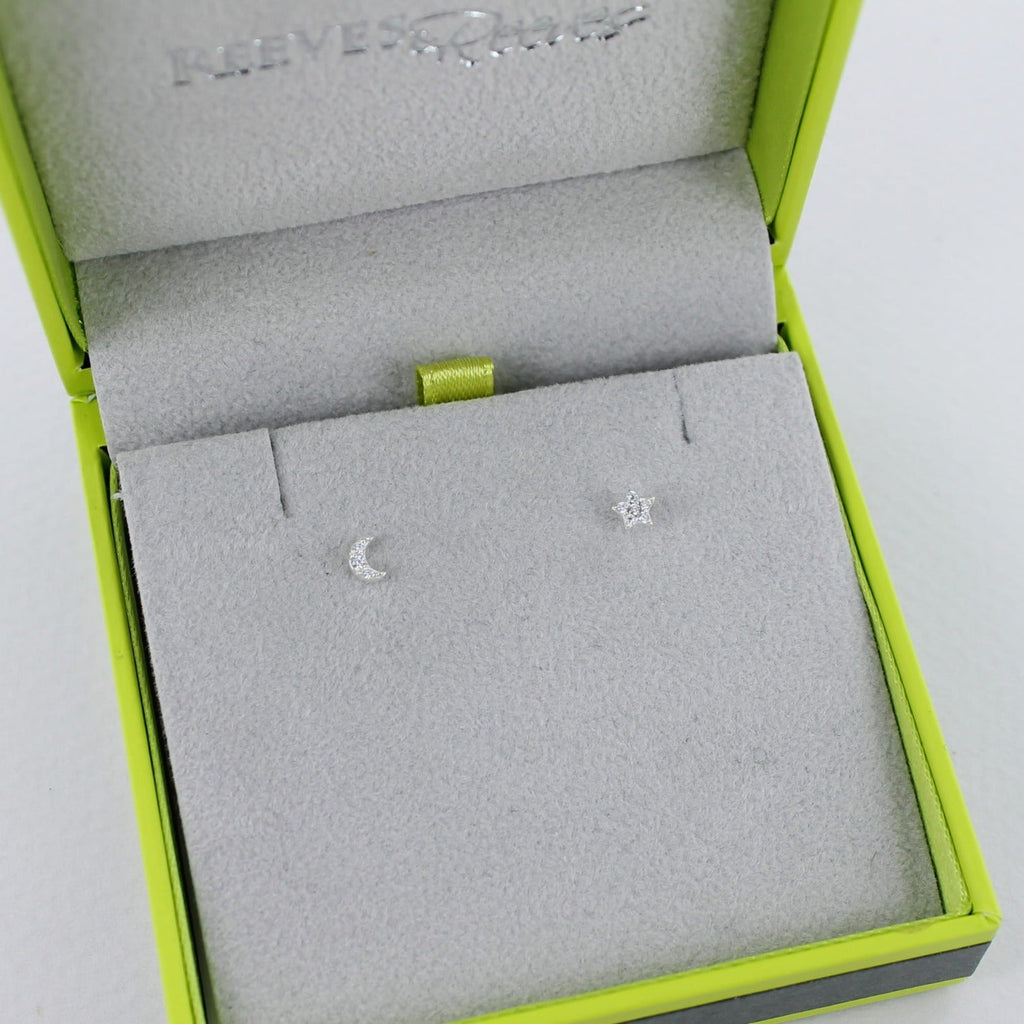 A pair of sterling silver mini moon and star stud earrings, shown in a Reeves & Reeves grey and green gift box.