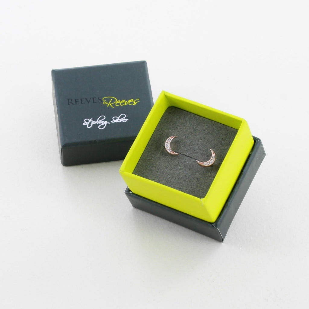 A pair of moon stud earrings in sterling silver with 18ct rose gold finish and cubic zirconia stones, shown in a Reeves & Reeves gift box.