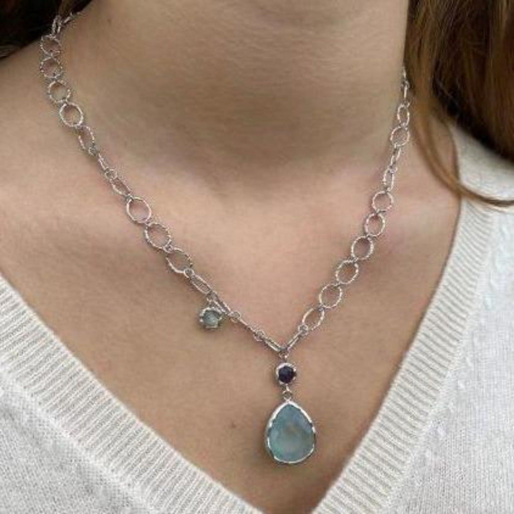 A sterling silver oval paper link style chain with textured finish on the ovals. Hanging from the centre is an amethyst stone, and below a larger peardrop aqua chalcedony stone. There is also a moonstone hanging further up the chain. Worn on a model.