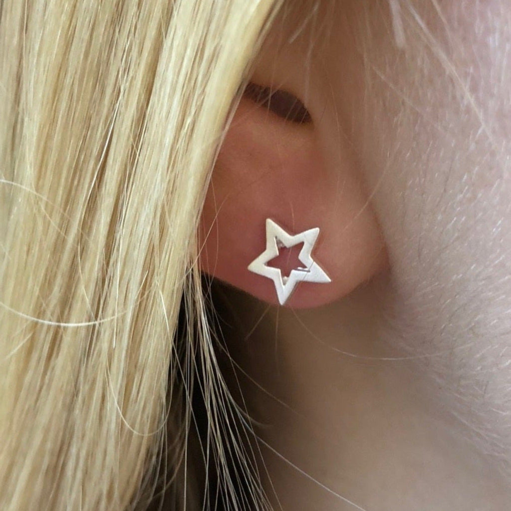 A sterling silver star silhouette stud earring, shown in a ladies ear.