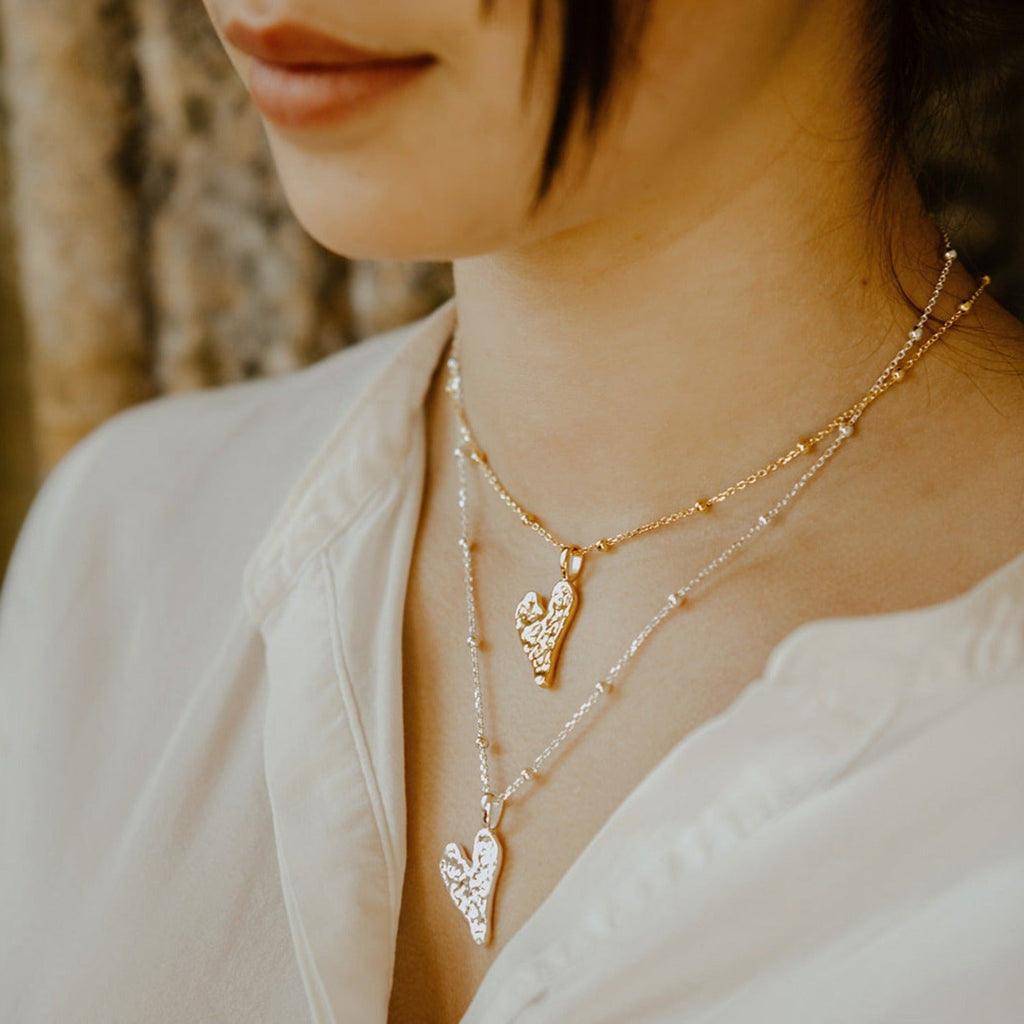 Silver and 18ct gold plate solid textured heart pendants, hanging on silver beaded chains, worn on a models neck.