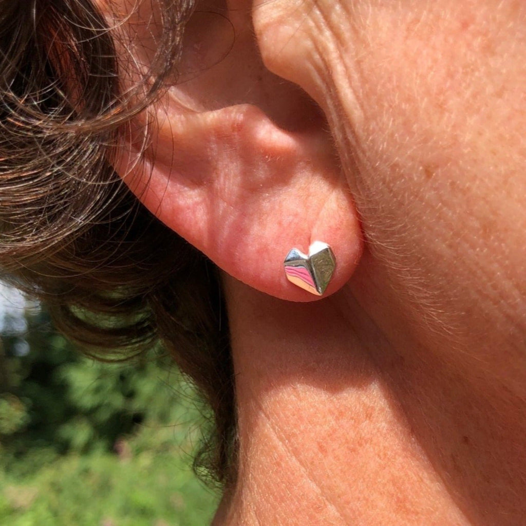 A sterling silver heart stud earring in an origami design, shown in a ladies ear.