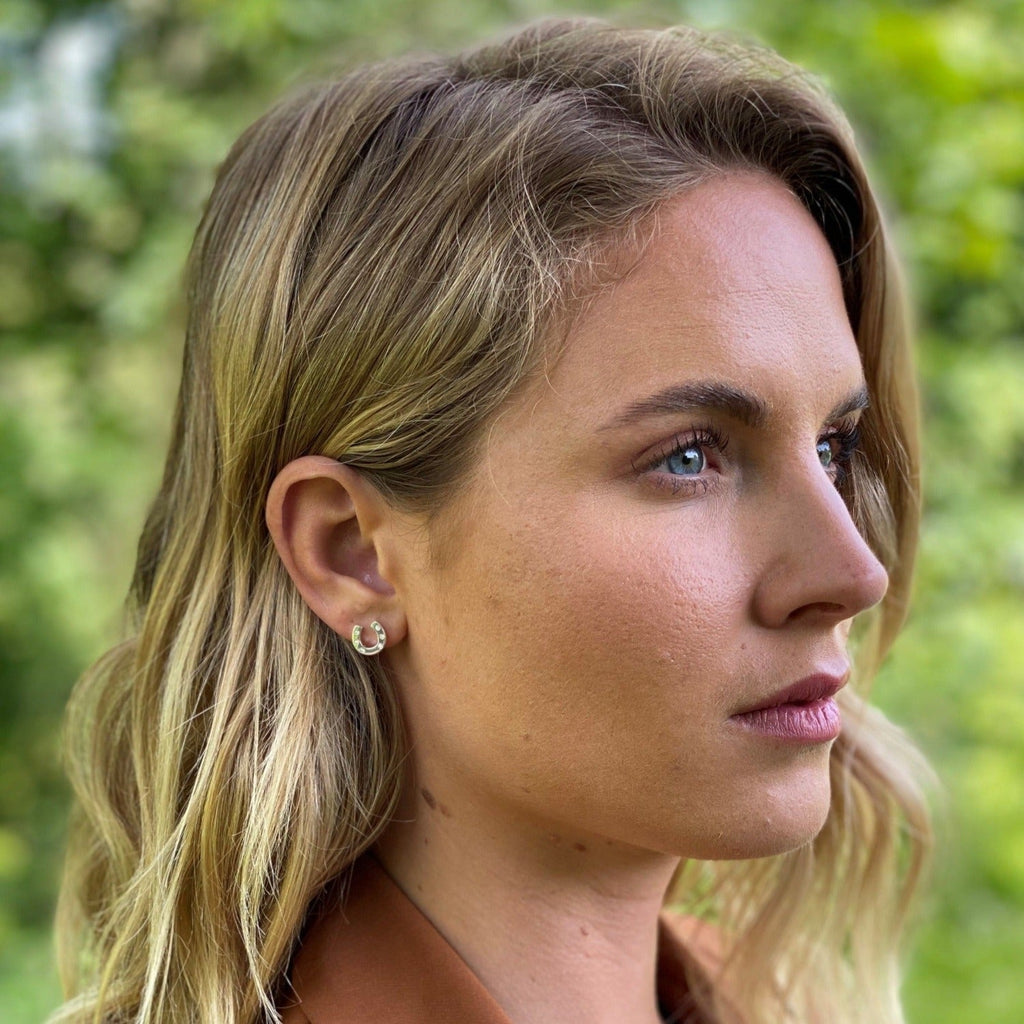 A sterling silver horseshoe stud earring with cubic zirconia stones, shown in a ladies ear.