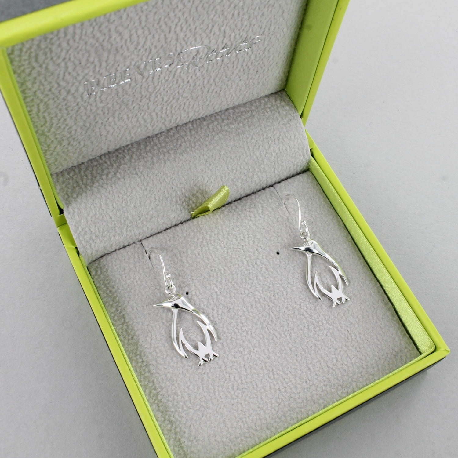 A pair of sterling silver penguin silhouette drop earrings, shown in a Reeves & Reeves gift box.