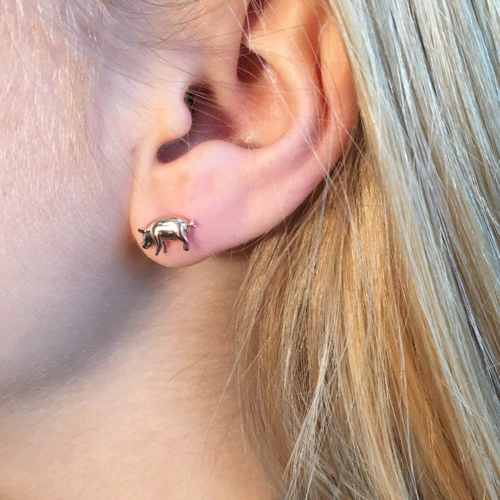 A sterling silver pig stud, shown in a ladies ear.