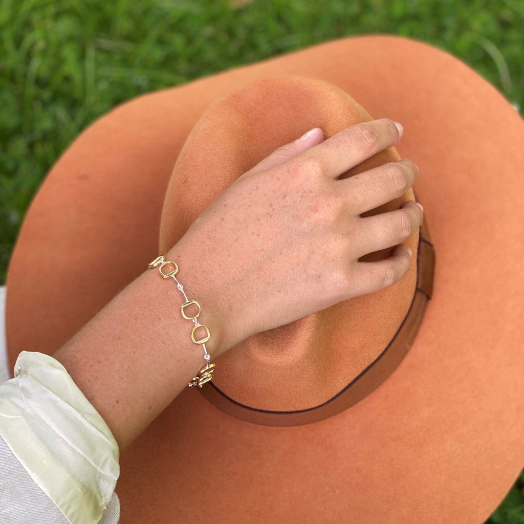 A sterling silver bracelet with gold plated detail, featuring four interlocking snaffle bits, worn on a wrist by a woman holding an orange coloured hat.