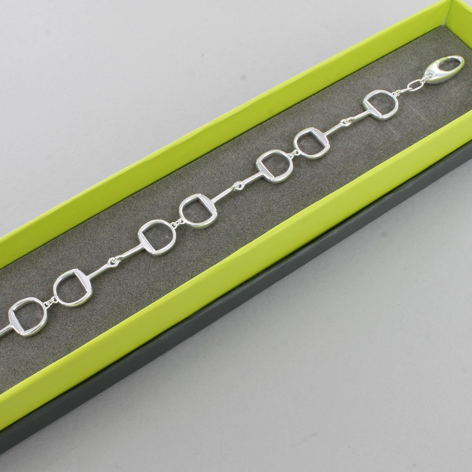 Sterling Silver Snaffle Bracelet with four interlocking snaffles and a lobster clasp, shown in a Reeves & Reeves grey and green branded gift box.