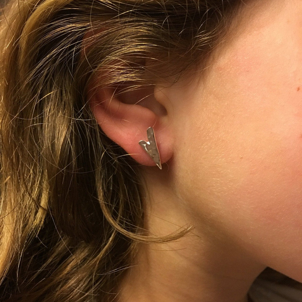 A sterling silver irregular heart stud earring with a hammered finish, shown in a ladies ear.