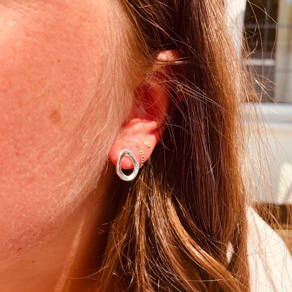 A sterling silver stud earring, in an irregular circular shape, shown in a ladies ear.