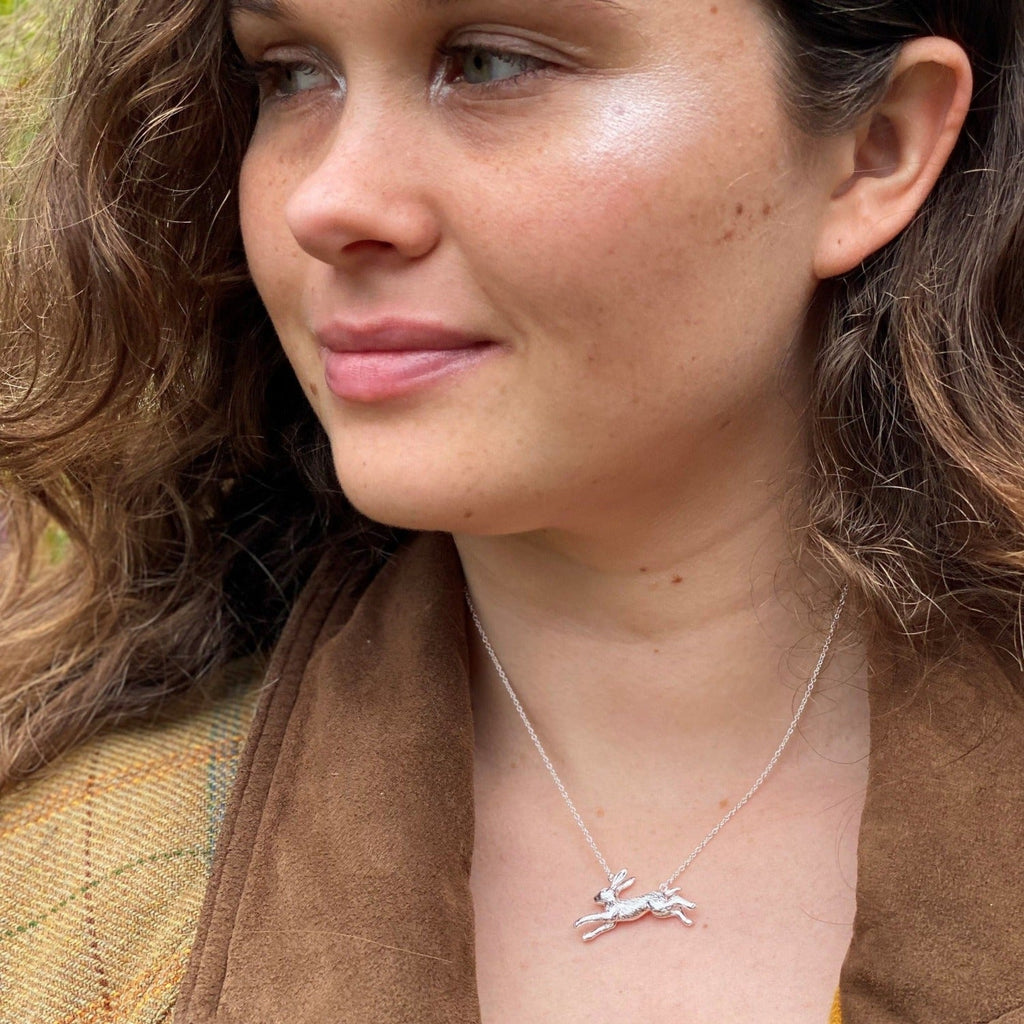 A Silver Running Hare Necklace on an adjustable silver chain, worn on a models neck.