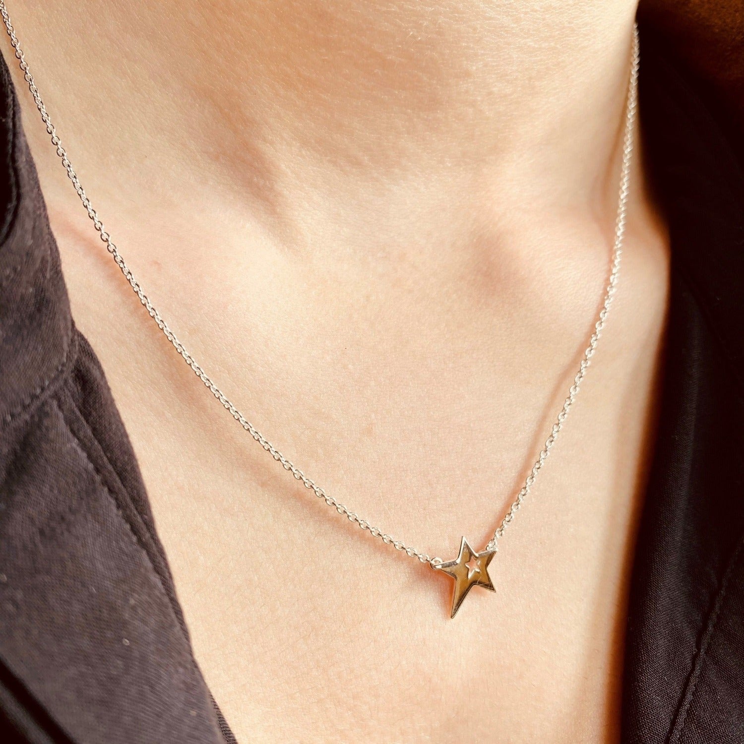 Star necklace with a cut out centre, hanging centrally on a sterling silver adjustable chain on a models neck.