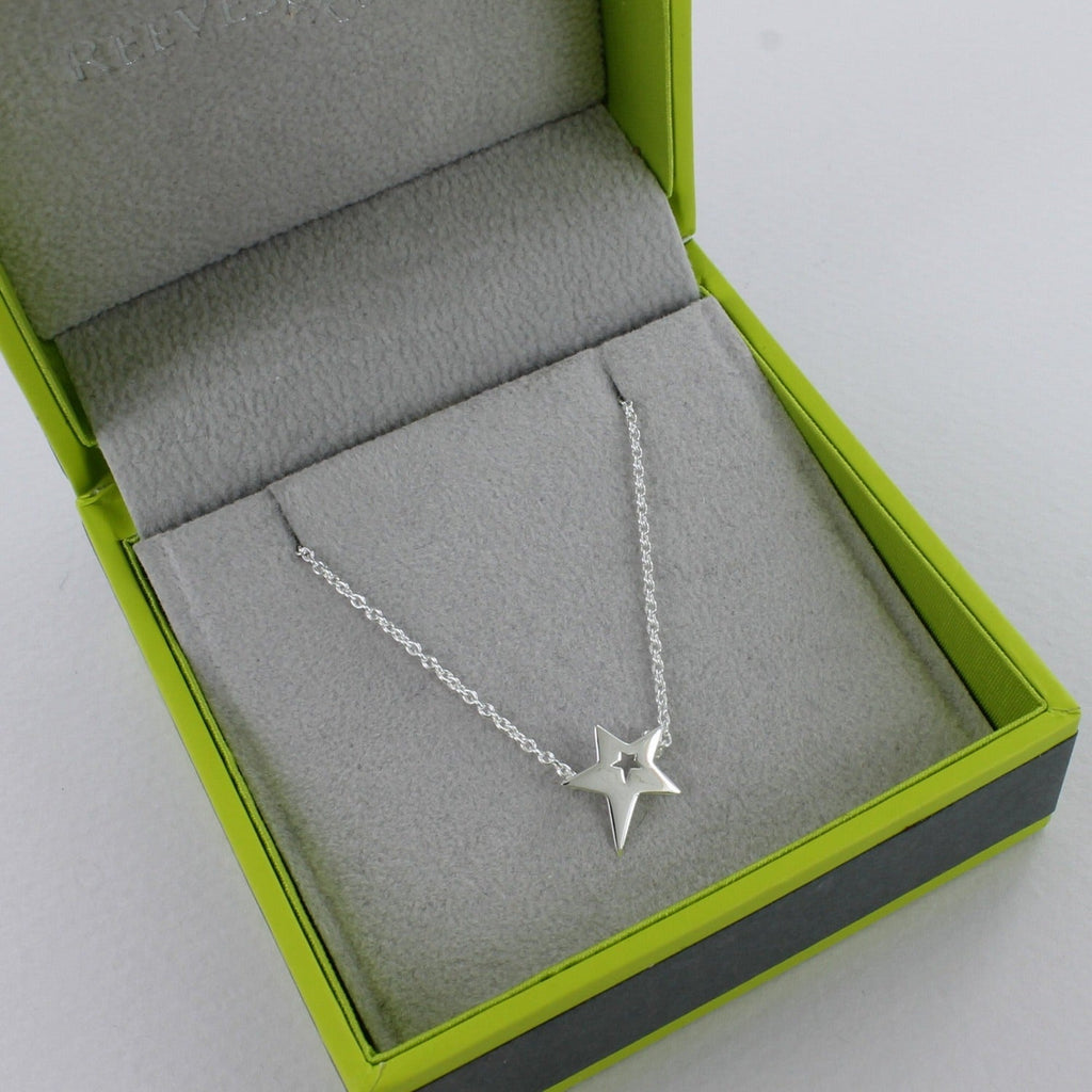 Silver star necklace with a cut out centre, hanging on a silver adjustable chain and in a Reeves & Reeves grey and green branded gift box.