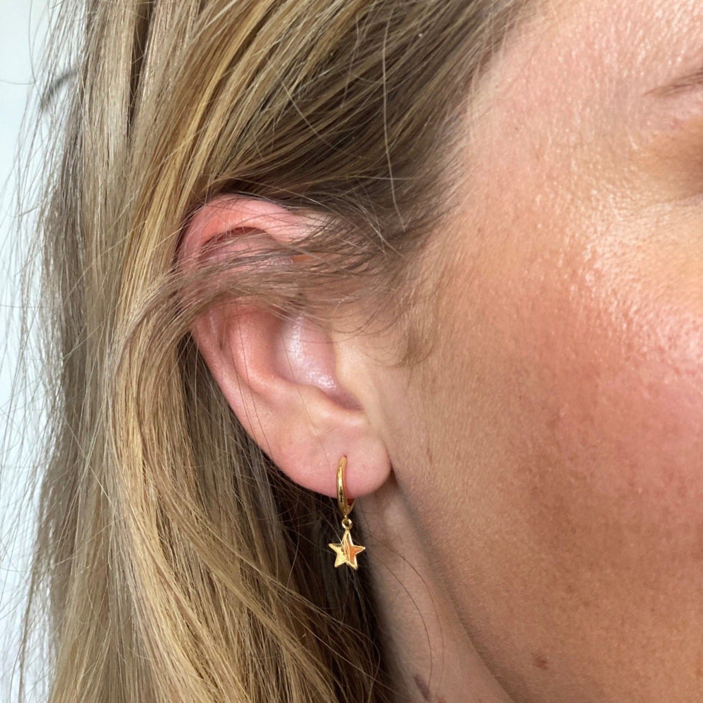 A sterling silver hoop earring with 18ct gold plating and a star charm hanging from the bottom. Shown in a ladies ear.
