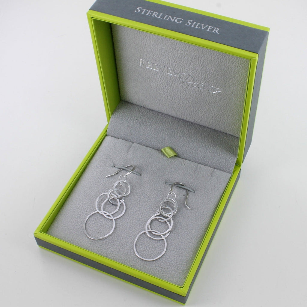 A pair of sterling silver drop style earrings, made of interlinking flat circles in a waterfall style effect. Hung on silver hooks and shown in a Reeves & Reeves gift box.