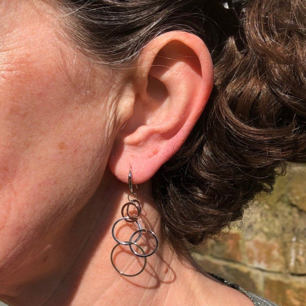 A sterling silver drop style earring made of interlinking flat circles, hanging on silver hooks and worn in a ladies ear.