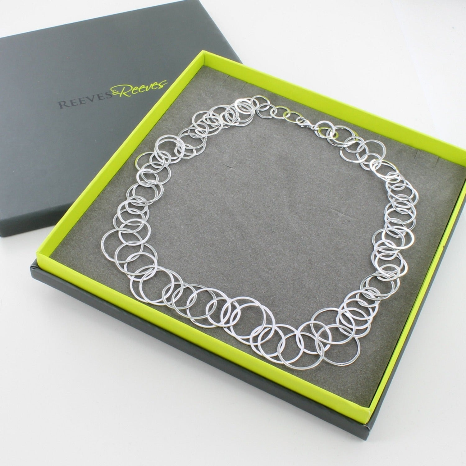 Sterling Silver Slinky Necklace made up of lots of intertwined circles and shown in a Reeves & Reeves grey and green branded gift box.