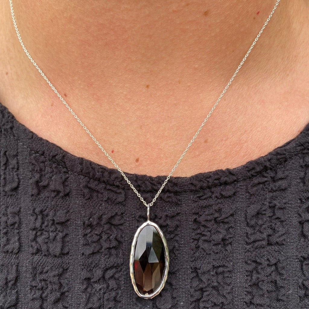 A sterling silver oval shaped smokey quartz stone, set in sterling silver and hung on a silver chain, worn on a model.