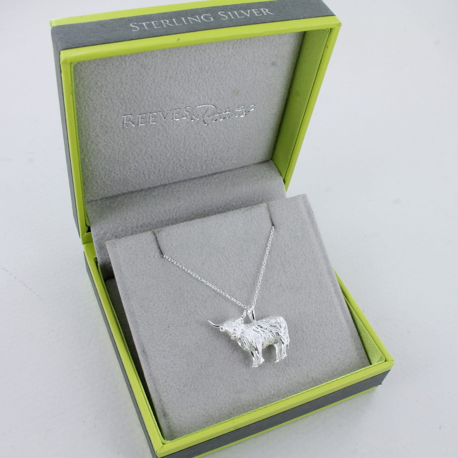 A Sterling Silver Highland Cow Necklace, on an adjustable silver chain, shown in a reeves and reeves branded gift box with grey and green colours.