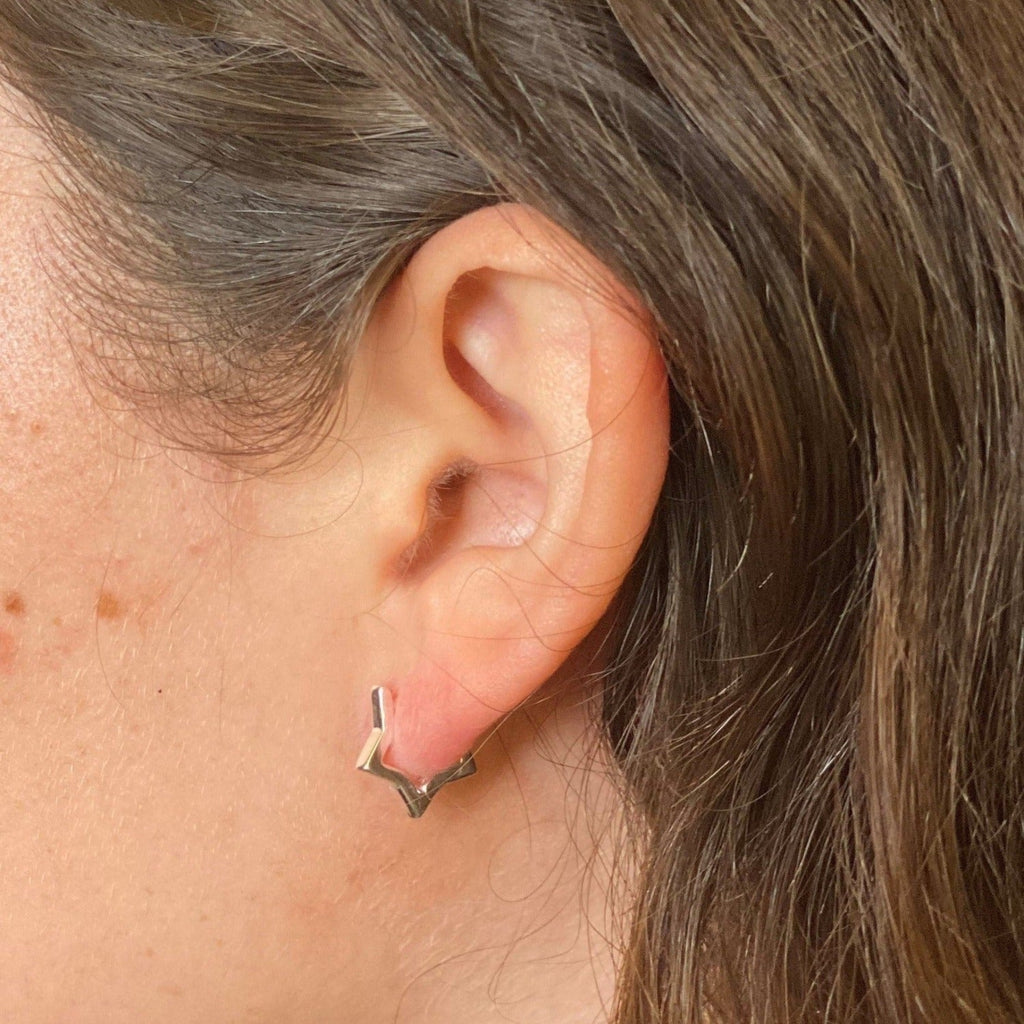 A sterling silver star shaped huggie, worn in a ladies ear.