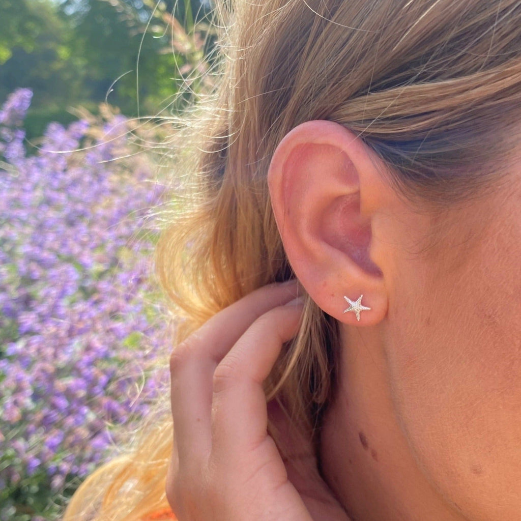 A sterling silver starfish stud earring, worn in a ladies ear.