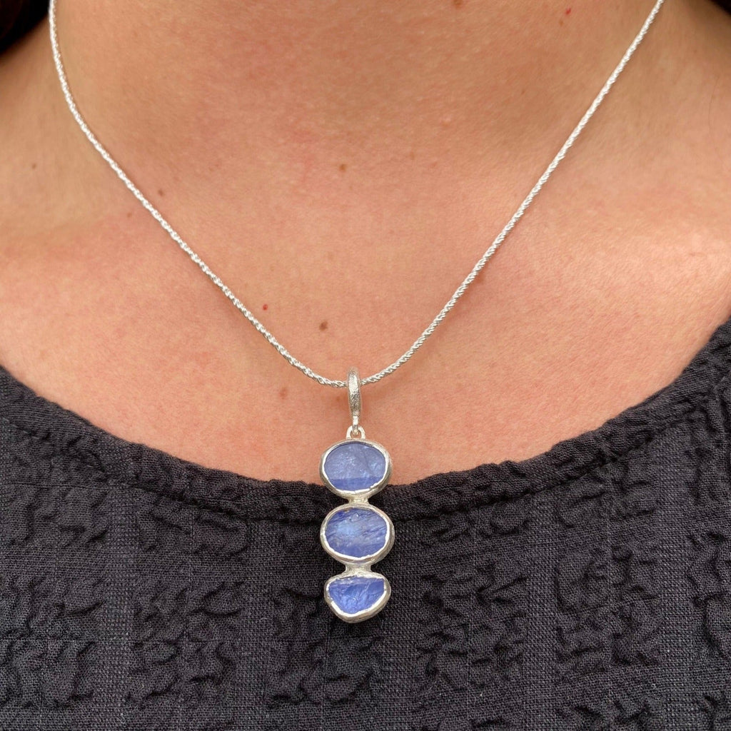 A sterling silver necklace with three tanzanite stones set in silver and hung in a vertical design. Hung on a silver rope style chain and worn on a model.