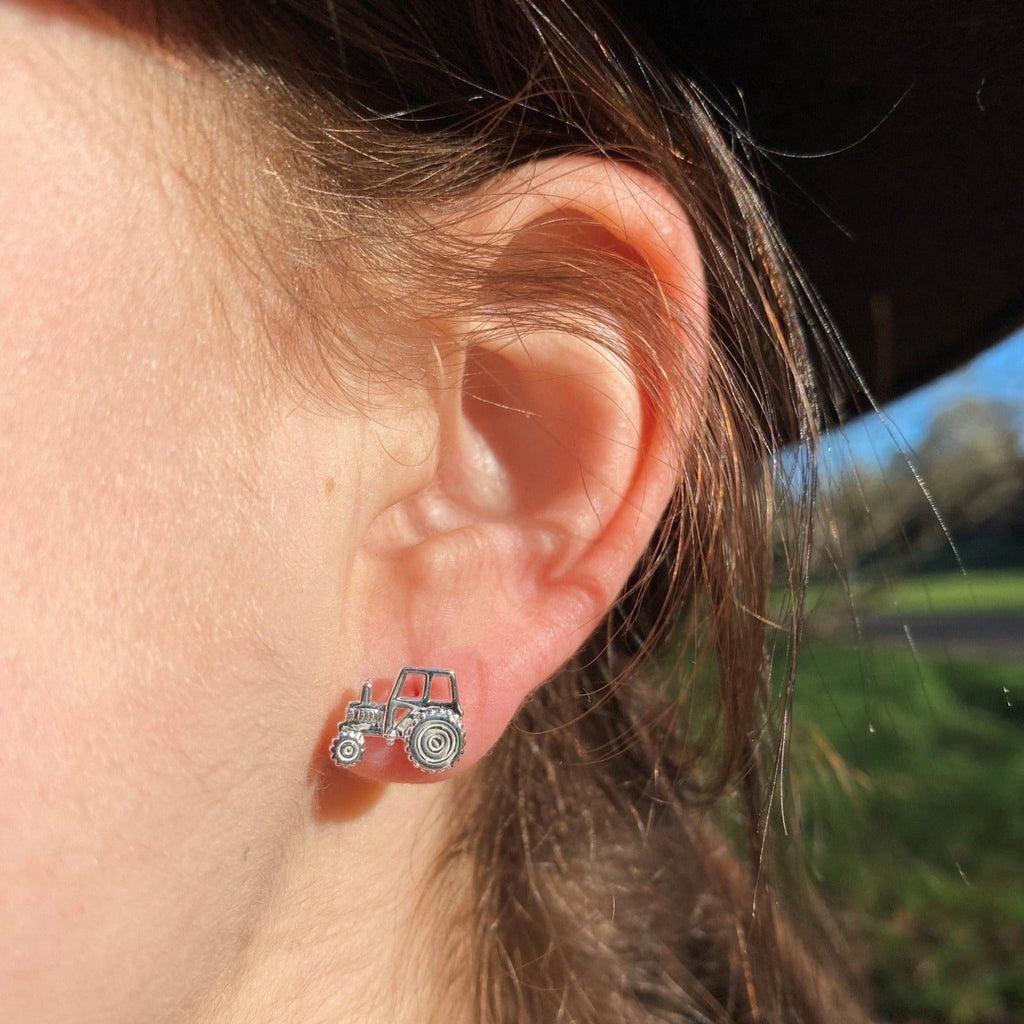A pair of sterling silver two dimensional Tractor stud earrings, shown in a ladies ear.