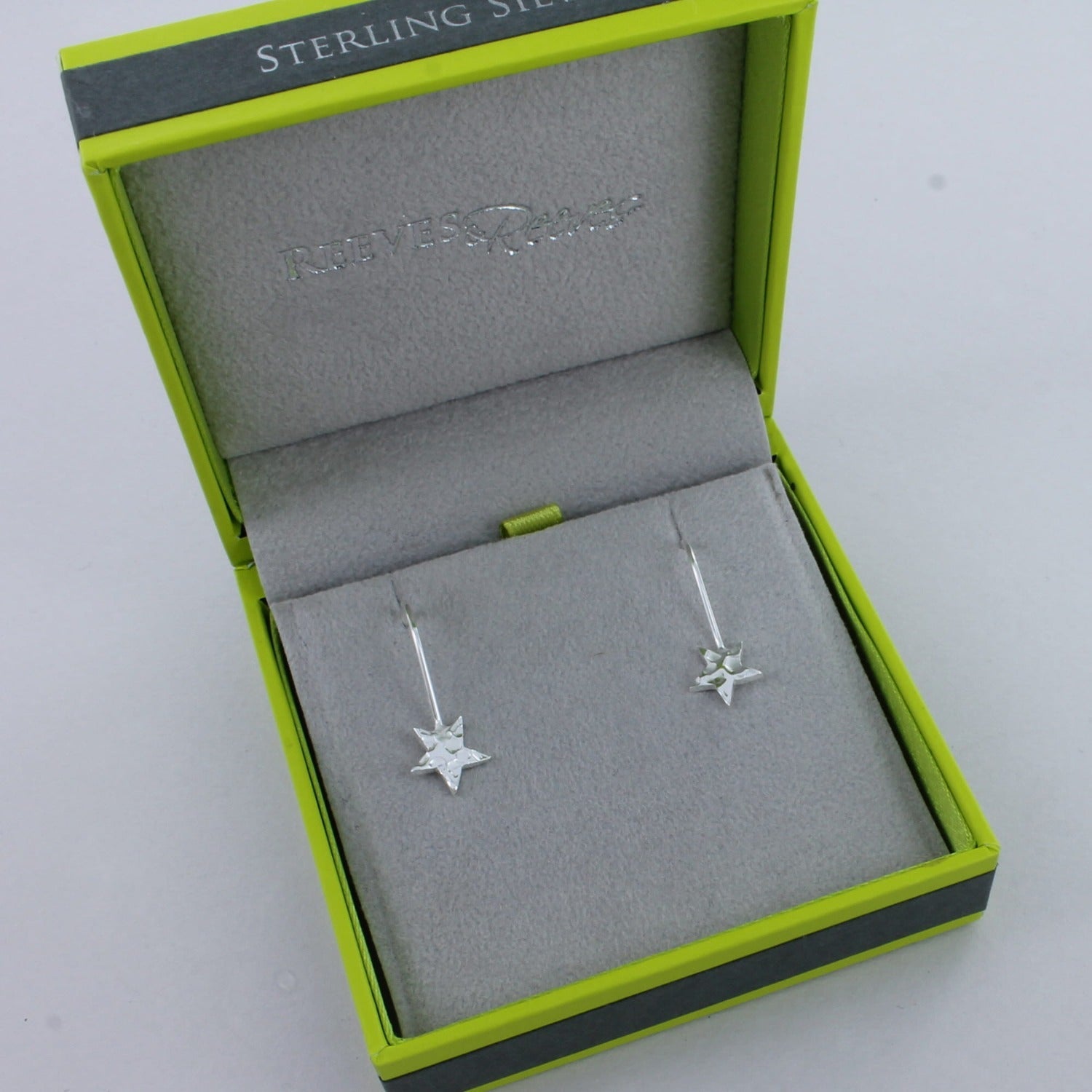 A pair of sterling silver drop earrings with hammered stars hanging from the bottom. Shown in a Reeves & Reeves gift box.