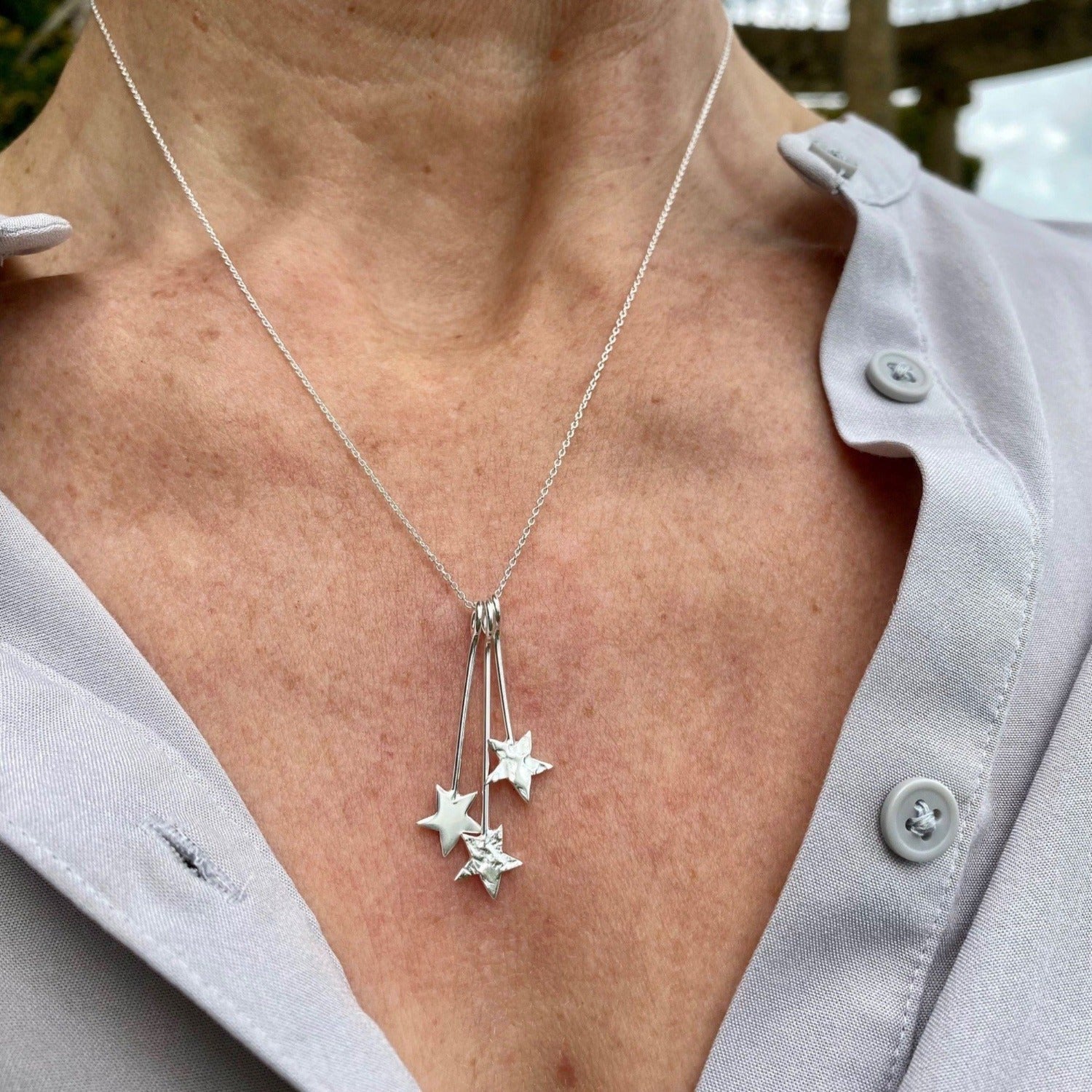 Three stars of varying textures hang from solid silver hooks which all hang from an adjustable silver chain. Worn on a models neck.