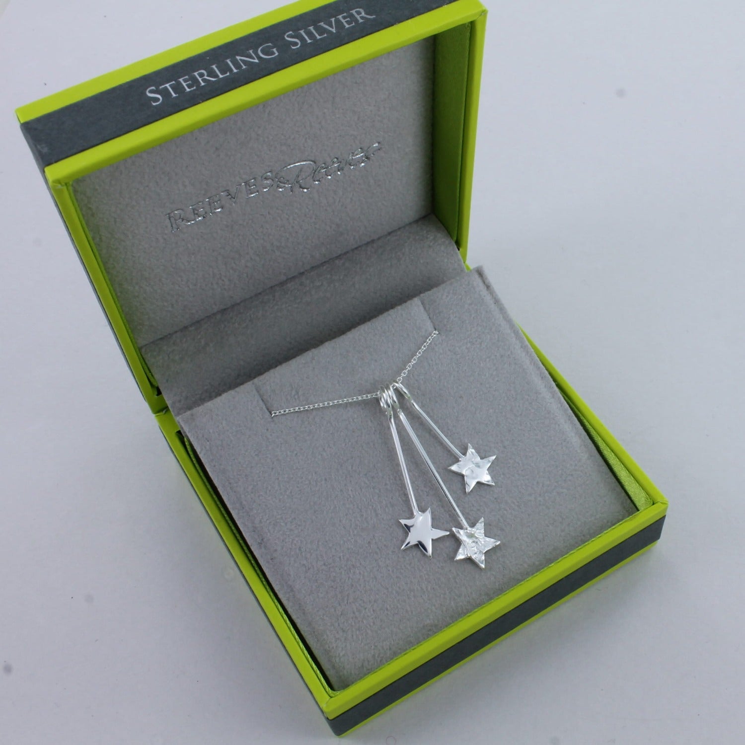 Three stars of varying textures hang from solid silver hooks on an adjustable silver chain. Shown in a Reeves & Reeves branded gift box.