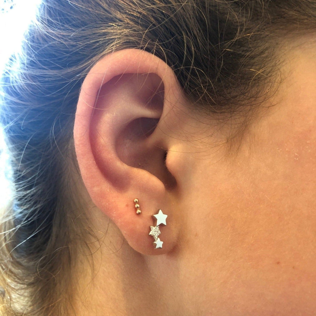 A sterling silver trio star stud earring, the stars are adjoined in a vertical line and the middle star is filled with cubic zirconia stones. Shown in a ladies ear.