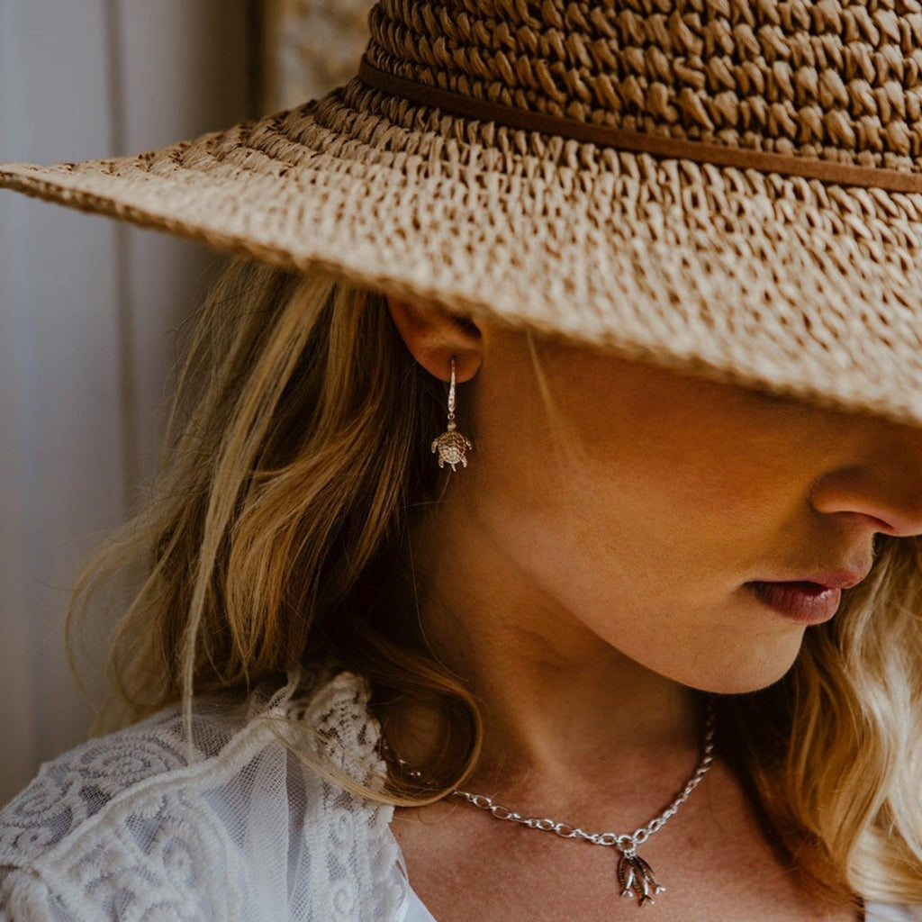 A Sterling Silver Turtle Earring hanging from a silver hammered hook and shown in a ladies ear.