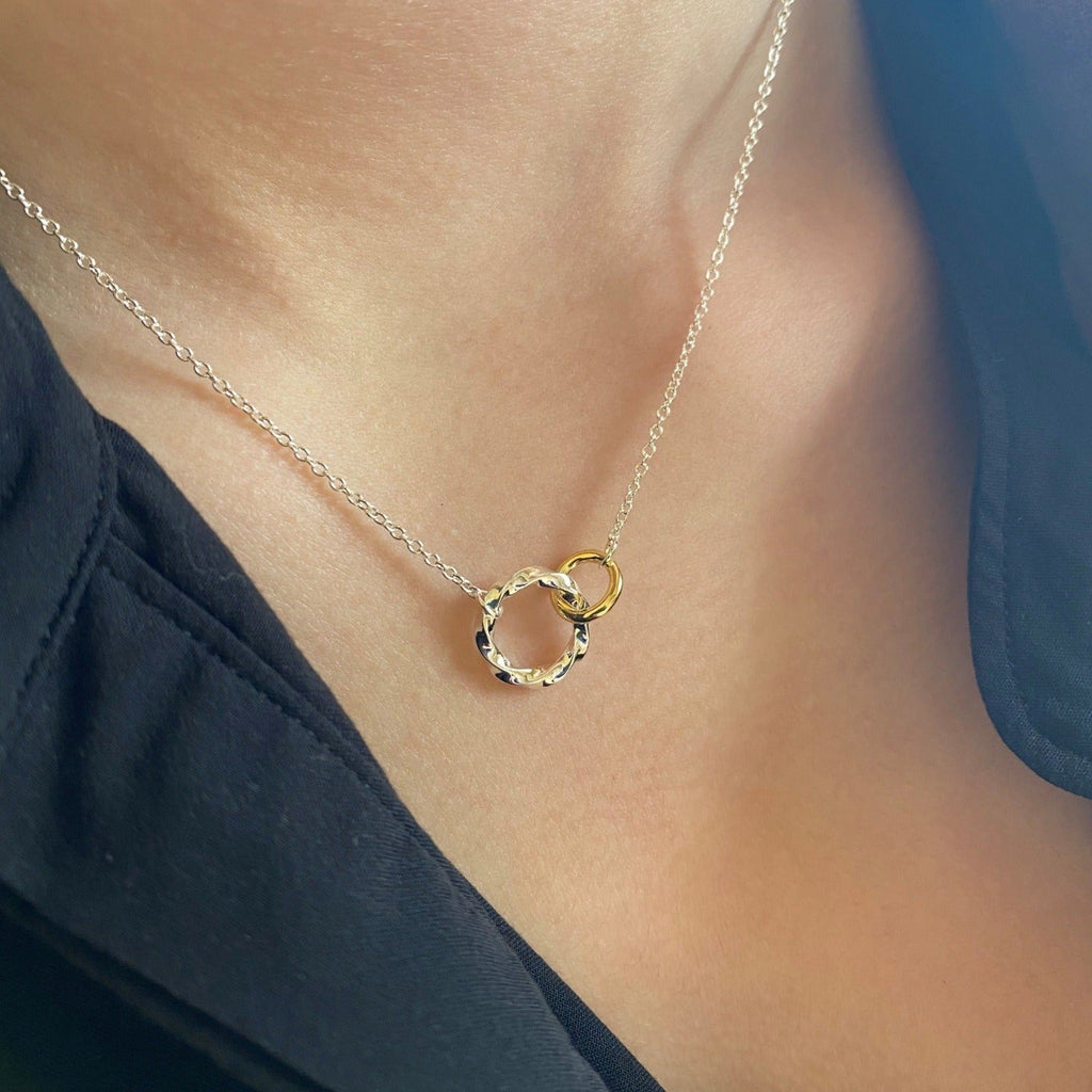 A sterling silver twisted circle silhouette with an interlinked gold plated smaller circle, both hanging centrally on a fine silver chain which is worn on a model.