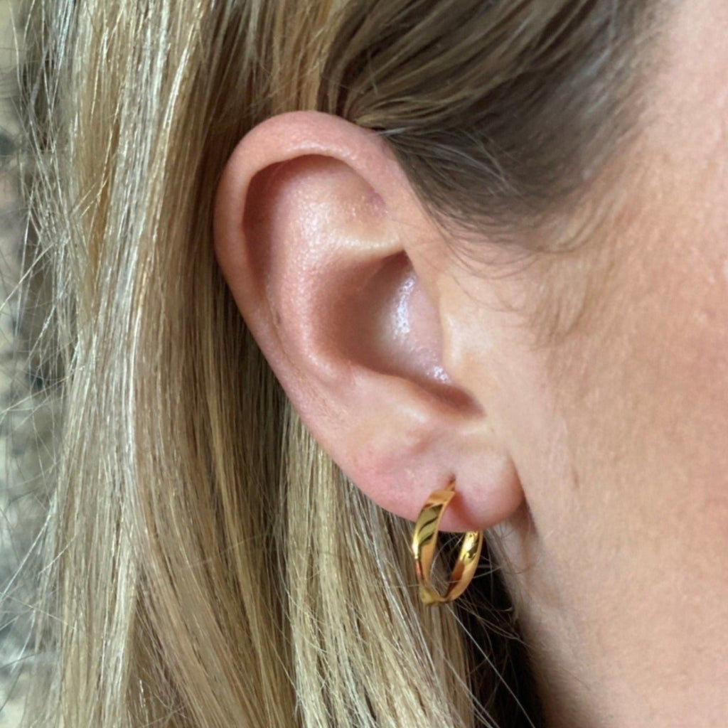 A twisted style hoop earring, in sterling silver with 18ct gold plate, shown in a ladies ear.
