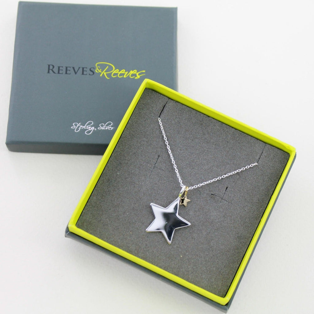 A silver large star with a smaller gold plated star hanging from a silver chain and shown in a Reeves & Reeves grey and green branded gift box.