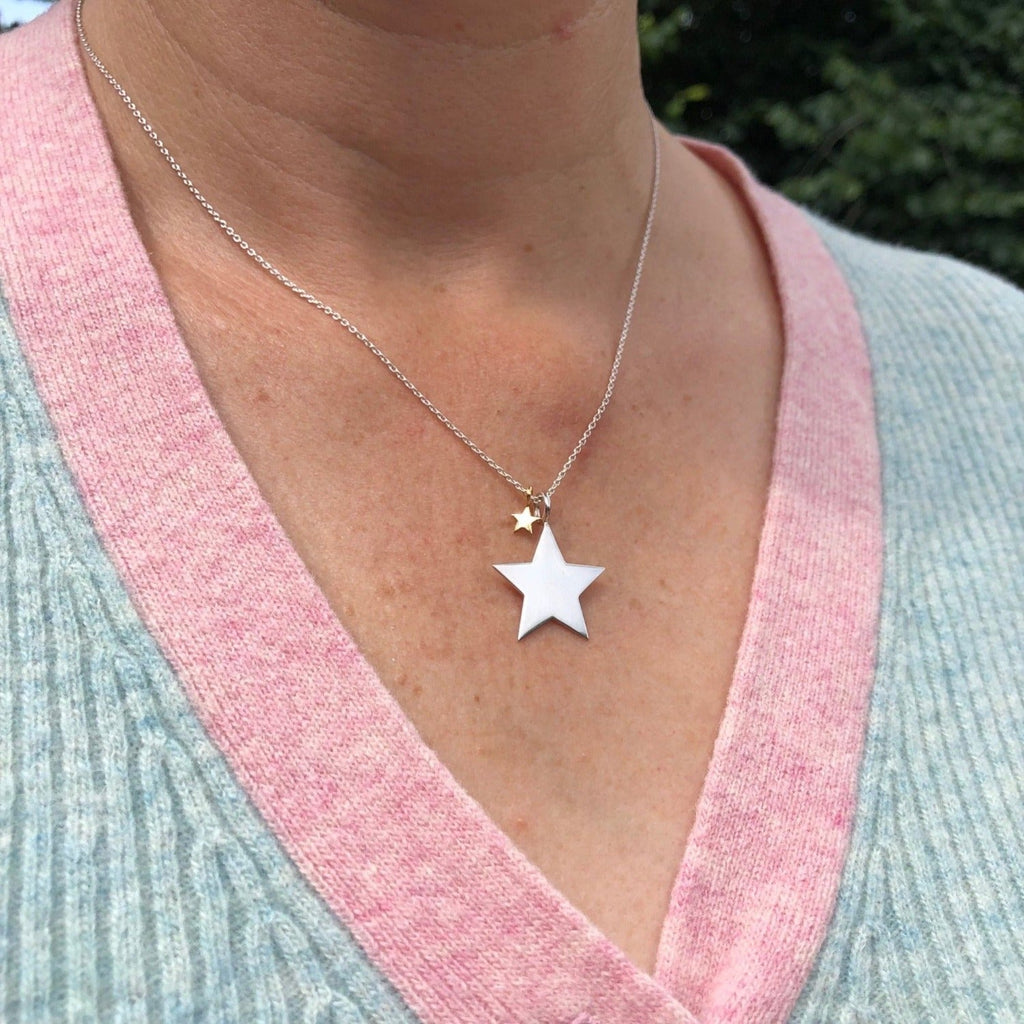 Silver large star pendant with a smaller gold plate star hanging from a silver chain and worn on a model.