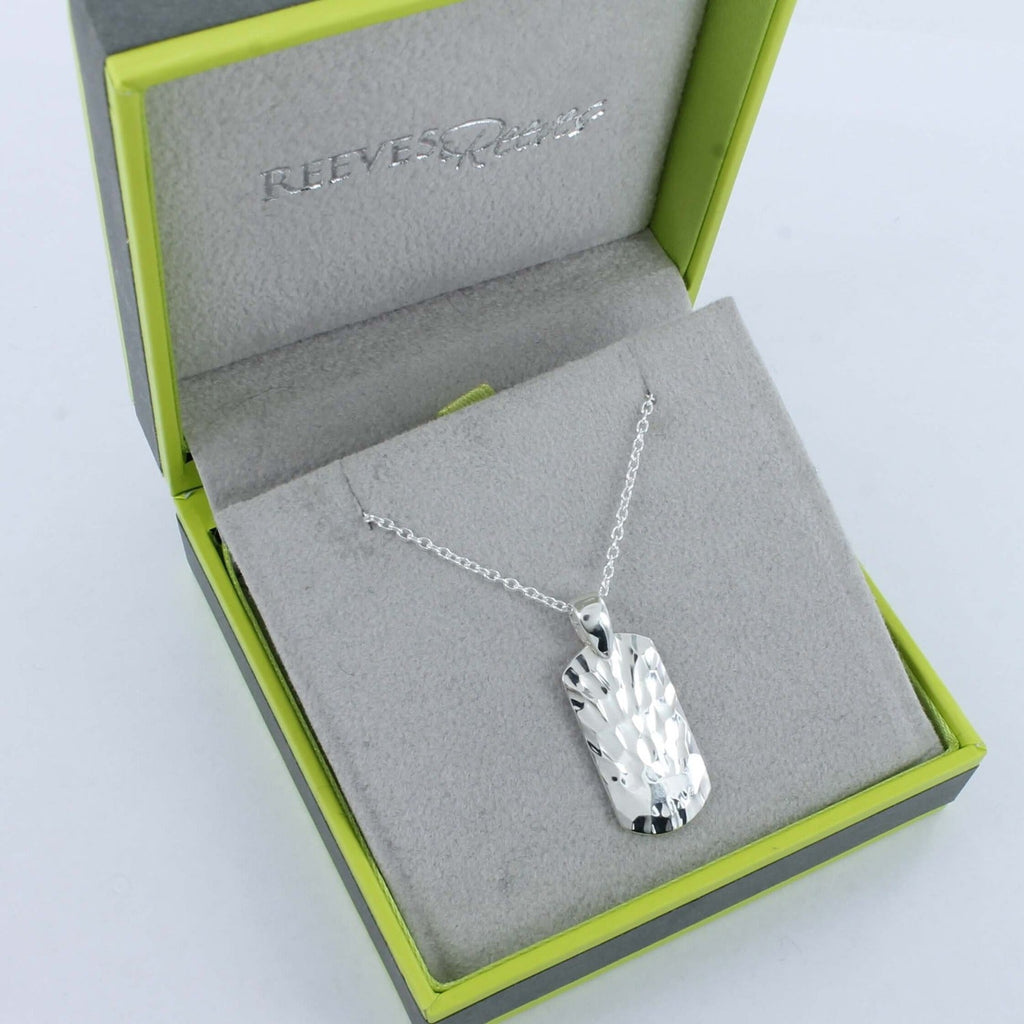 A textured dog tag pendant, rectangular in shape withs lightly rounded edges, hung on a silver chain and shown in a Reeves & Reeves grey and green gift box.