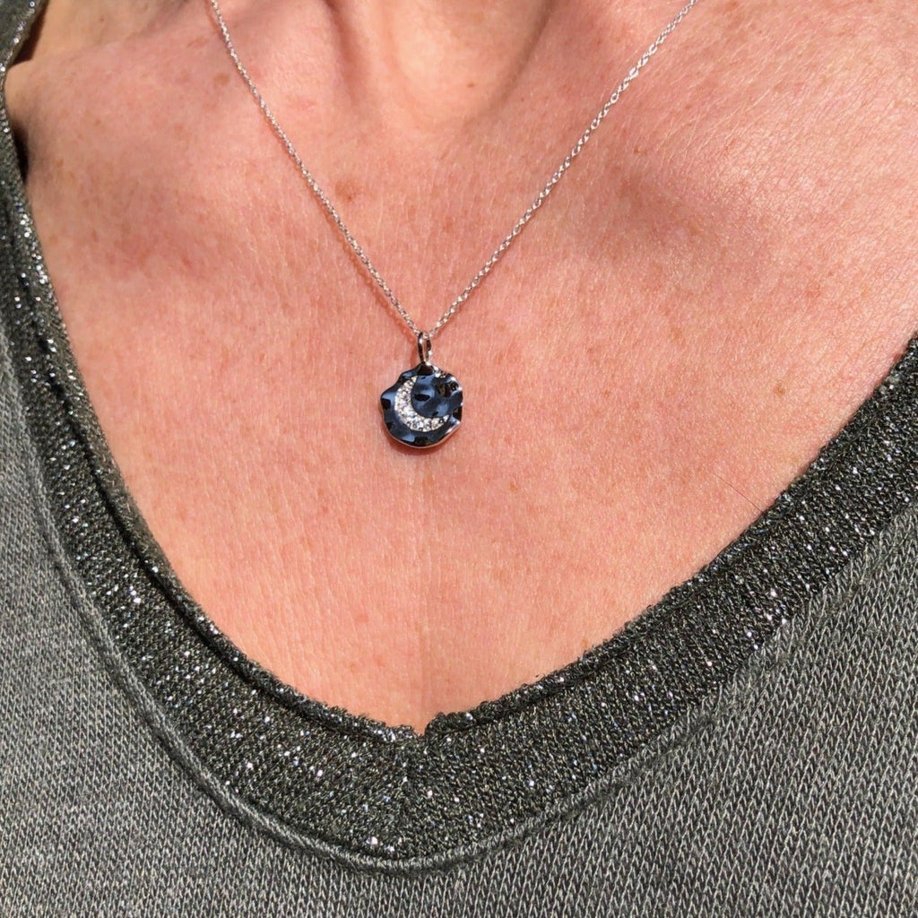 Textured Silver Disc Necklace with a moon in the centre which is filled with cubic zirconia stones. Hangs on an adjustable silver chain and worn on a models neck.